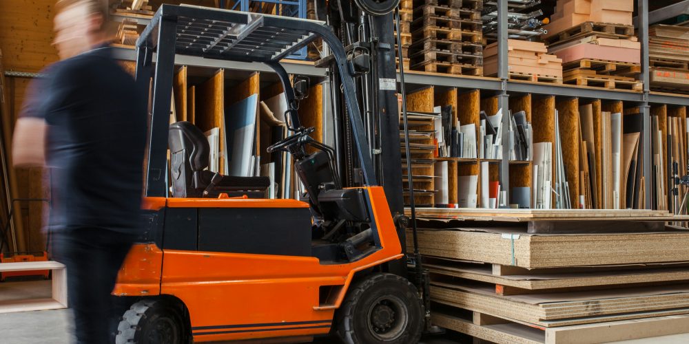 Worker with a forklift in a large carpentry workshop with many timbers in the background.