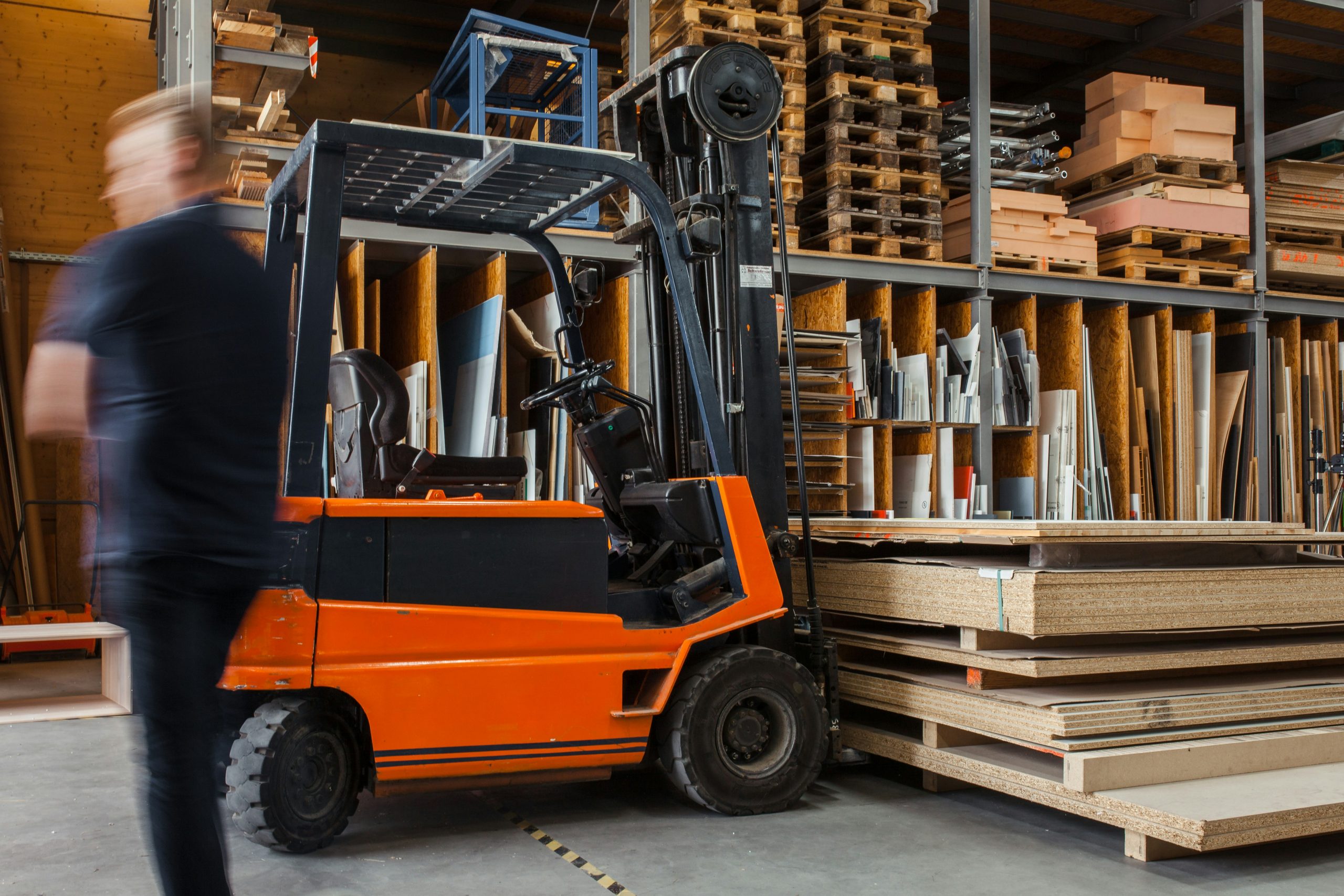 Worker with a forklift in a large carpentry workshop with many timbers in the background.